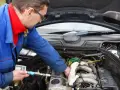 Mechanik w niebieskim kombinezonie sprawdza silnik diesla, używając przyrządu.