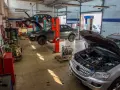 Warsztat samochodowy z kilkoma autami na podnośnikach, w tym ciemnym sedanem, który wygląda jak p1351 peugeot. Silnik wyjęty z jednego z pojazdów.