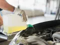 Ręce w rękawiczkach nalewają żółty płyn z kanistra do silnika samochodu. To może być płyn chłodniczy lub płyn do spryskiwaczy, ważny dla prawidłowego działania g12++.