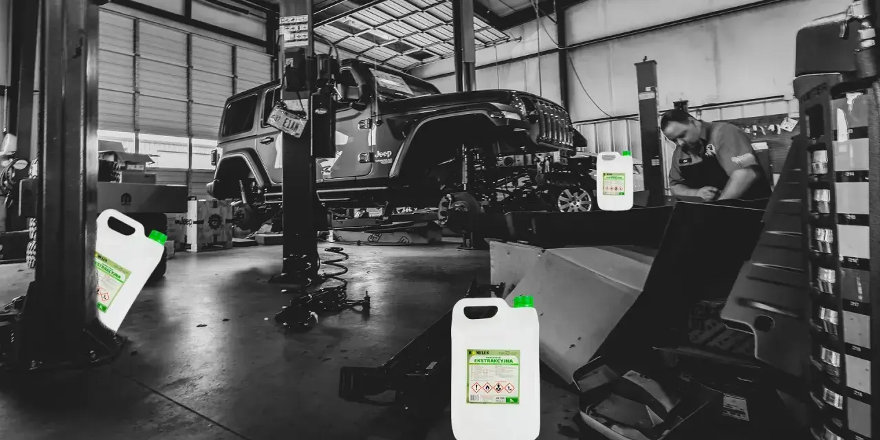 Warsztat samochodowy, Jeep na podnośniku, mechanik pracuje. Na pierwszym planie kanistry z napisem "benzyna ekstrakcyjna".