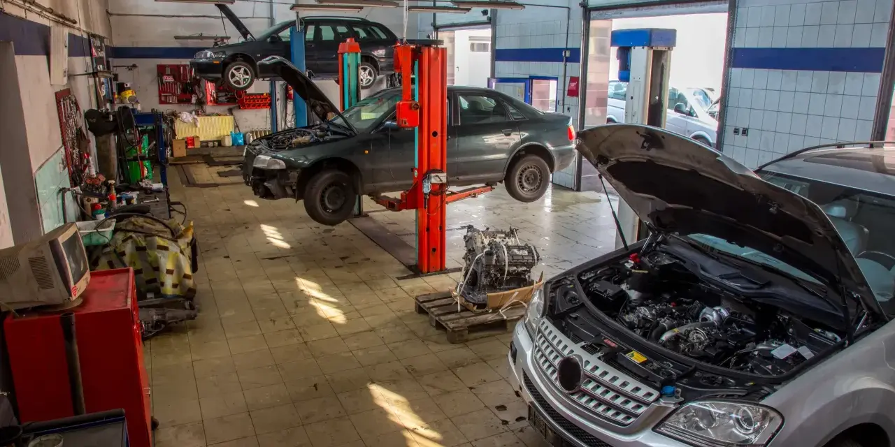 Warsztat samochodowy z kilkoma autami na podnośnikach, w tym ciemnym sedanem, który wygląda jak p1351 peugeot. Silnik wyjęty z jednego z pojazdów.