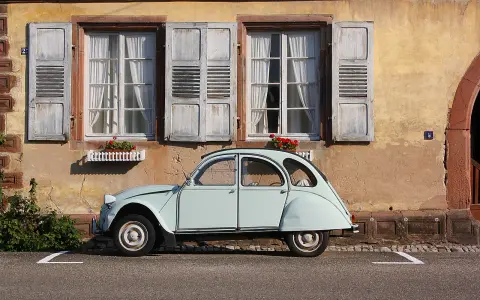 Jasnoniebieski, zabytkowy Citroen 2CV, jeden z klasycznych modele stare, parkuje przed kamiennym domem z drewnianymi okiennicami.