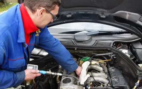 Mechanik w niebieskim kombinezonie sprawdza silnik diesla, używając przyrządu.