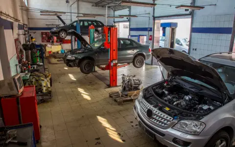 Warsztat samochodowy z kilkoma autami na podnośnikach, w tym ciemnym sedanem, który wygląda jak p1351 peugeot. Silnik wyjęty z jednego z pojazdów.