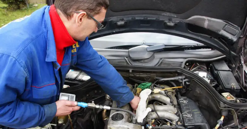 Mechanik w niebieskim kombinezonie sprawdza silnik diesla, używając przyrządu.